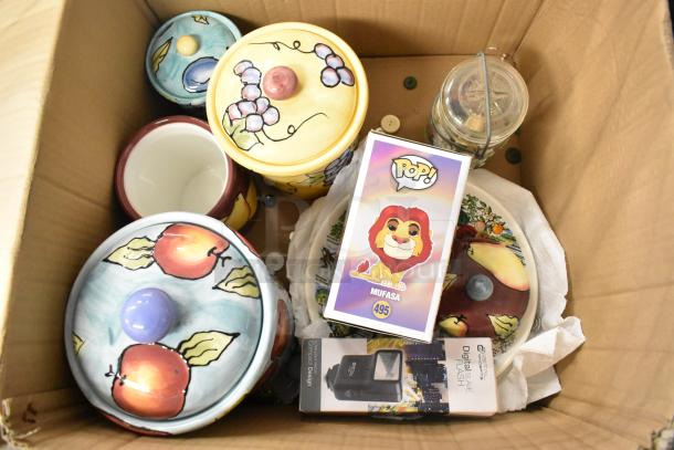 Boxed lot of items featuring colorful ceramic containers with fruit designs, a Mufasa Funko Pop, and a digital camera flash.