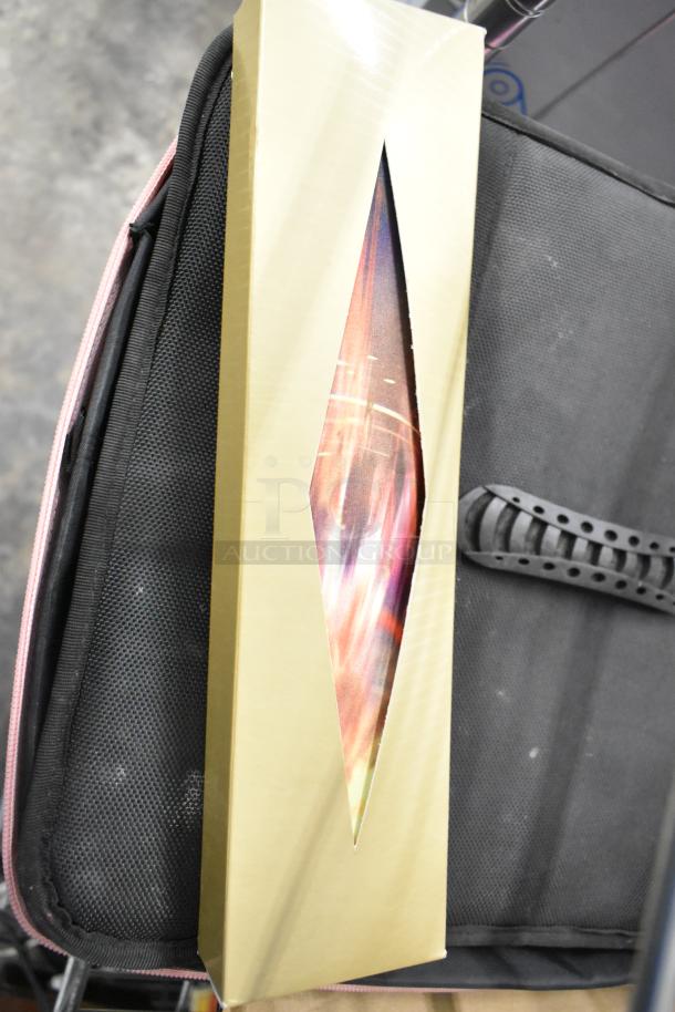 A gold box with a tapered window showing colorful details, leaning against a black fabric case.