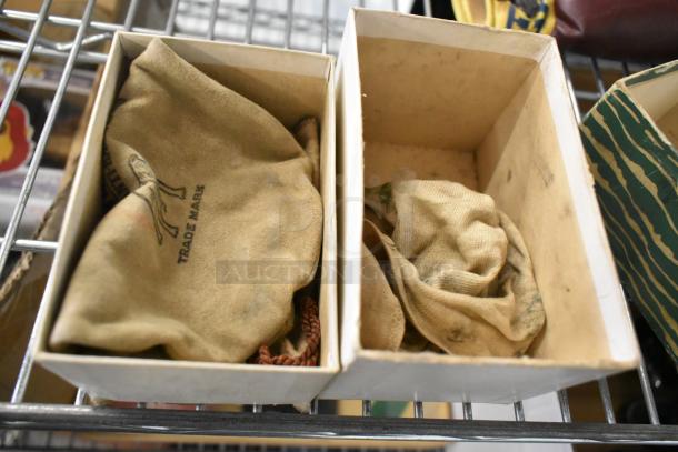 Boxes containing wrapped items, possibly ceramic containers or state plates, in worn fabric pouches marked "Trade Mark."