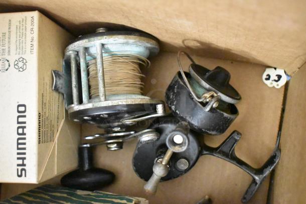 Box containing vintage fishing reels with attached line, a Shimano item box with branding, all in used condition.