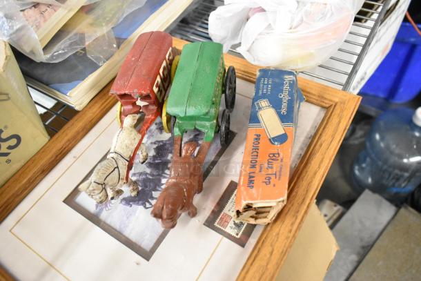 Tiered lot of vintage items including figurines, Pez dispensers, two horses and wagons, and boxed Westinghouse projection lamp.