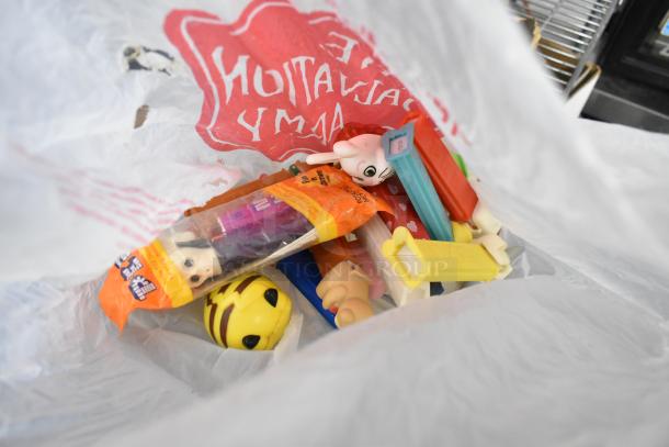 Assorted items including Pez dispensers, figurines, and toys visible in a plastic bag, featuring a vibrant mix of colors and characters.