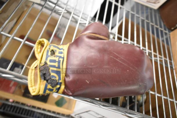 Worn maroon boxing glove with a yellow label on the cuff. Visible wear and tear on the label. Part of a mixed auction lot.