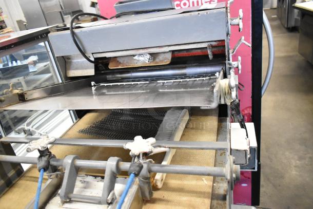 Metal commercial floor dough sheeter with adjustable rollers; visible wear but operational, suitable for bakery use.