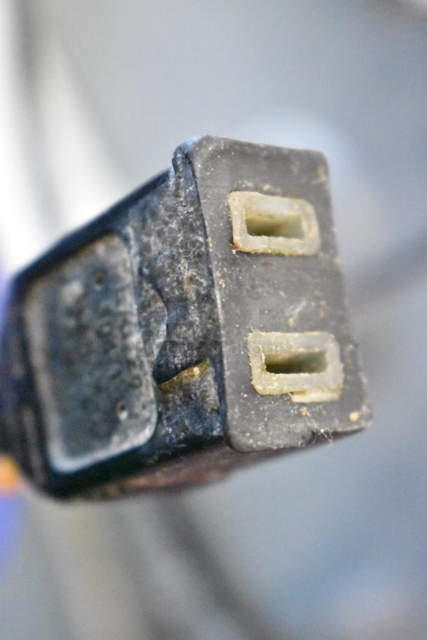Close-up detail of a power plug from a metal commercial floor style dough sheeter, showing two prongs and signs of wear.