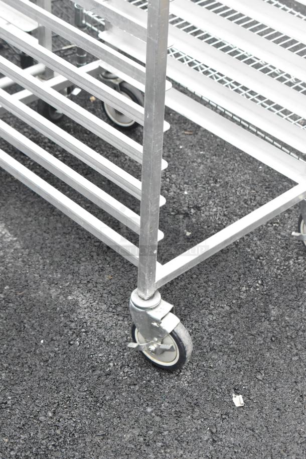 Two metal commercial pan transport racks on casters, featuring multiple slotted shelves for storage, in used condition.
