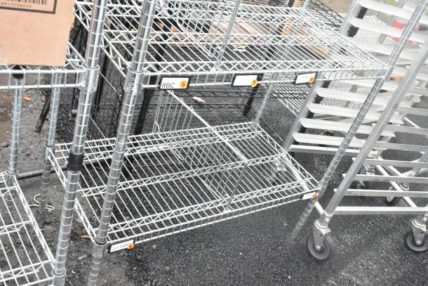 Chrome finish 4 tier wire shelving unit on wheels, requires buyer dismantling, visible "RBC" label on metal frame.