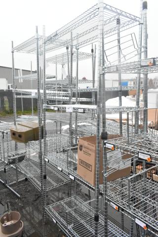 Chrome finish 4-tier wire shelving unit outdoors. Labels and tags visible on shelves. Buyer must dismantle for shipping.