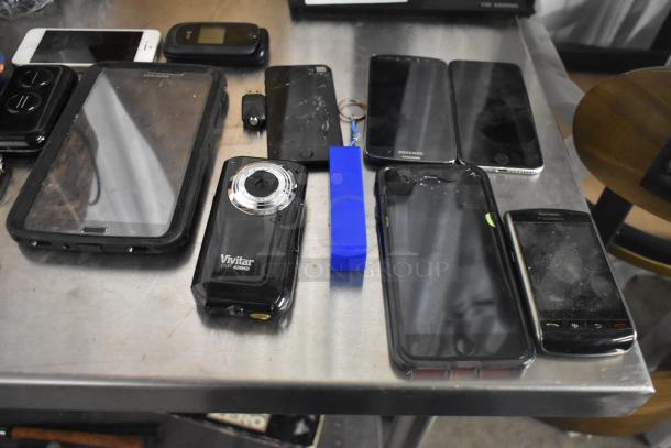 22 electronic items including phones, tablet, and a Vivitar DVR426HD camera on a table, various conditions.