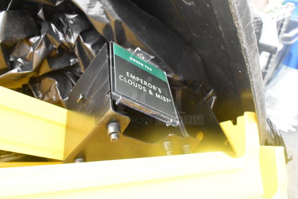Poly trash can with contents, including bread caddies. Features tea storage box labeled “Green Tea: Emperor’s Clouds & Mist.” Visible wear.