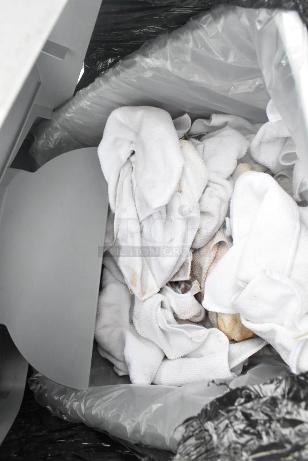 Poly trash can containing white towels; some towels show signs of use. Black and gray lining visible.