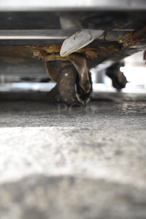 Delfield 406CA-DD1 undercounter cooler on worn commercial casters. Stainless steel, 115V, rust visible on casters.