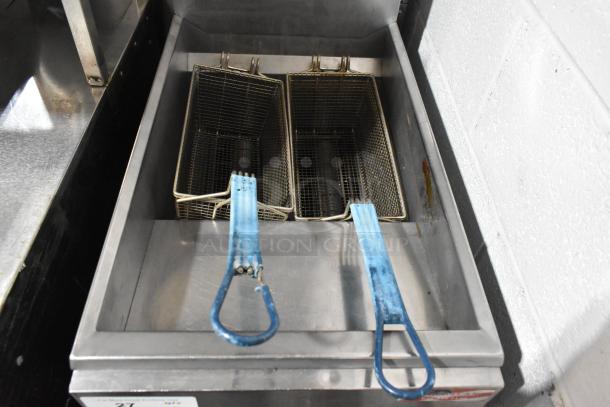 Stainless steel commercial floor-style deep fat fryer with two metal fry baskets, visible wear, suitable for restaurant use.