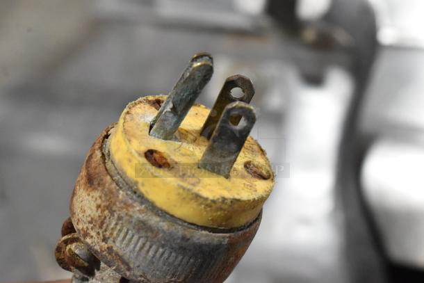 Rusty yellow electrical plug of Globe 500 meat slicer. Indicates wear. Item includes blade sharpener but missing carriage.