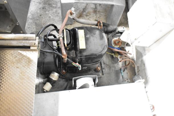 Commercial compressor with wire connections and metal casing, showing signs of wear. Yellow label with specifications visible.