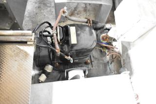 Commercial compressor with wire connections and metal casing, showing signs of wear. Yellow label with specifications visible.