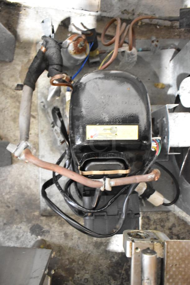Commercial compressor with black casing, copper tubing, and electrical wires. Visible label includes safety information. Good condition.