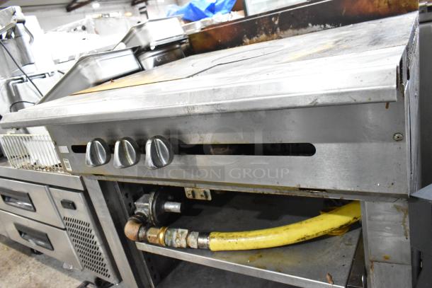 Stainless steel single burner French top range with gas power, two under shelves, commercial casters, and visible wear.