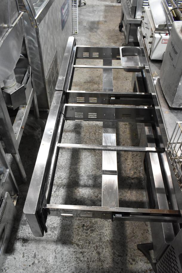 Stainless steel commercial 4-drawer chef base on casters, 115 volts, 1 phase, open drawers, industrial setting.