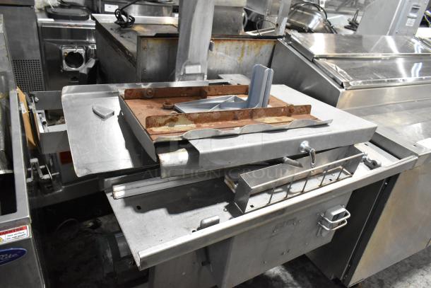 Metal commercial floor-style meat saw with a rusted base and stainless steel body. Used condition, features sliding tray and cutting guide.