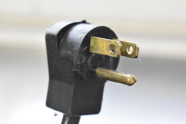 Close-up of a black electrical plug with three brass prongs, used for connecting appliances to power sources.