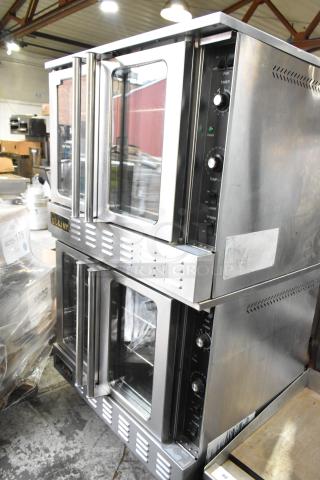 Dual L&J NY stainless steel convection ovens with glass doors, metal racks, thermostatic controls, on commercial casters.