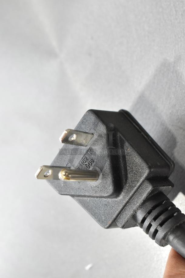 Close-up of a power plug from a Waring WSC165BX Crepe Maker, showing prongs and electrical markings.