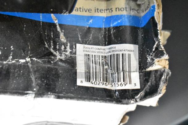 Damaged packaging for 3.2 cu. ft. compact fridge, stainless steel look, with visible barcode and product label.