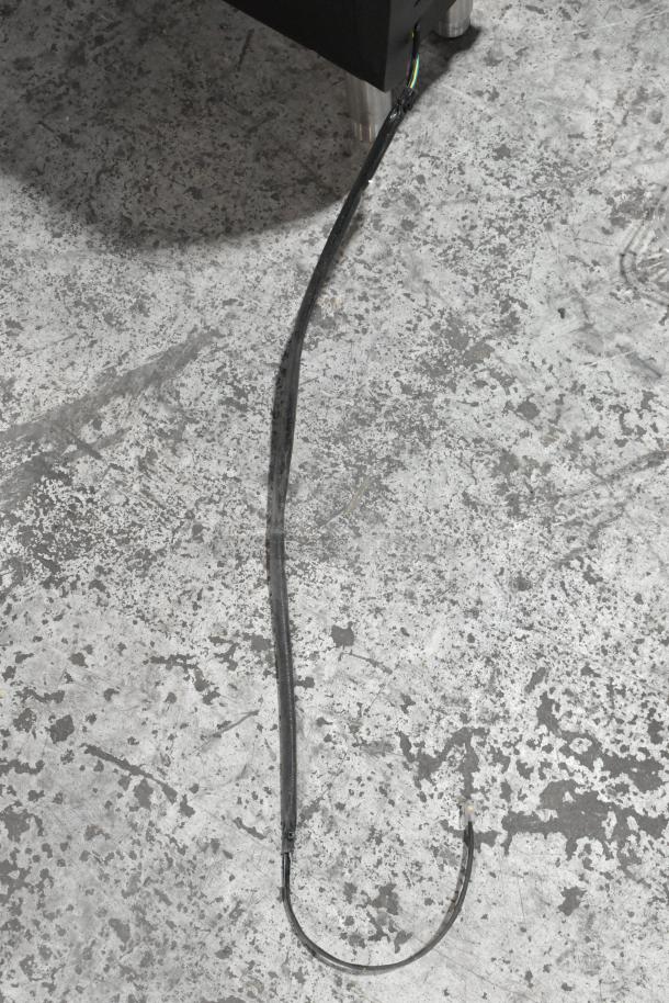 Metal flavor dispenser with attached tubing on a textured floor. Condition appears used. No visible tags or markings.