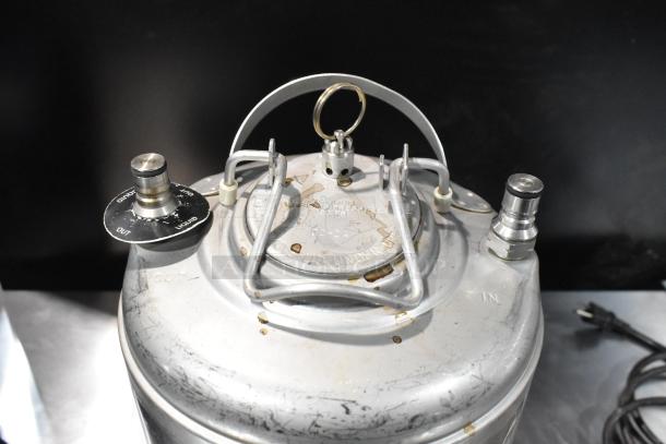 Vintage metal homebrew keg with "IN" and "OUT" valves, secure lid with handles, and visible wear. Durable brewing equipment.