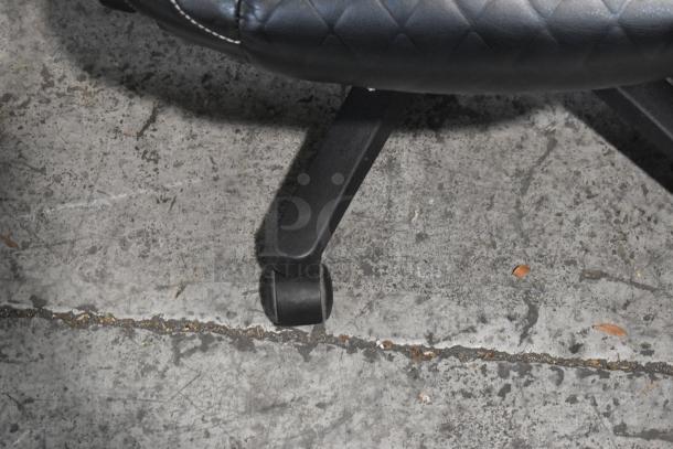 Alt text: Office chair caster on concrete floor, showing a black leather upholstery with white stitching.
