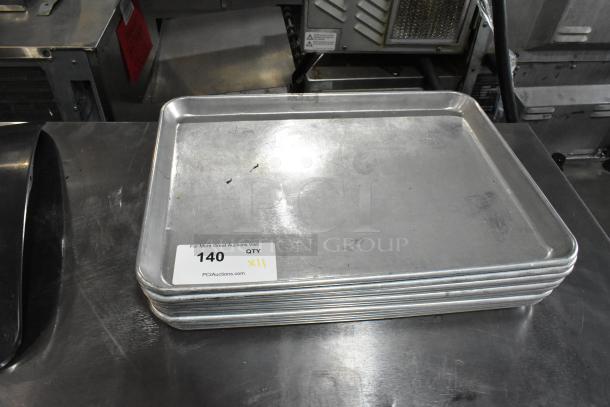 11 metal baking pans, stacked, used condition. Auction tag reads "140" and "QTY XII" from PCIAuctions.com.