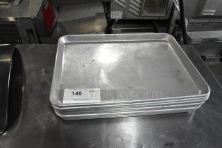 11 metal baking pans, stacked, used condition. Auction tag reads "140" and "QTY XII" from PCIAuctions.com.