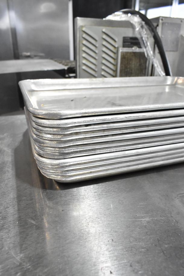 Stack of 11 metal baking pans with smooth, slightly worn surfaces, indicating light use.