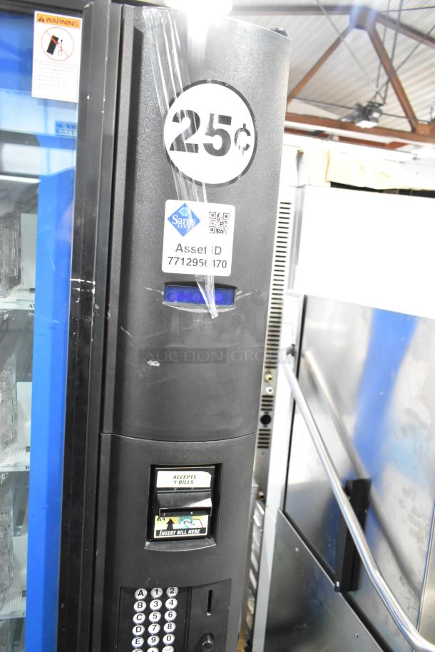 Metal commercial vending machine with bill acceptor, showing scratches and wear. Features keypad, 25-cent price label, Sam's Club asset ID.