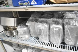 Tiered lot of various stainless steel drop-in bins, wrapped in plastic, including model 4070349. Stored on metal shelves.