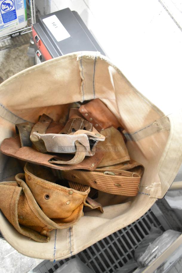 A canvas bag filled with assorted leather tool belts and straps, part of a mixed auction lot.