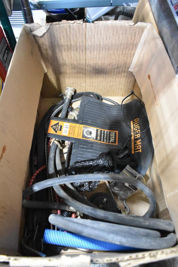 Cardboard box with assorted items: hoses, rope, outlet covers, Rugged Mat. Mixed condition, ideal for DIY projects.
