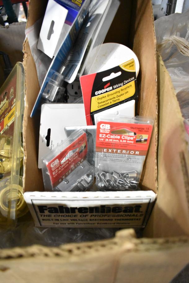 Box of assorted items, including Cooper wiring devices, Gardner Bender EZ-Cable Clips, outlet covers, and more, in original packaging.