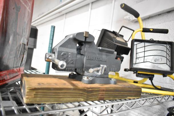 Lot of items including a Craftsman 3 1/2" bench vise on a wood base, SM2262 magnetic base worklight, and other tools on a shelf.
