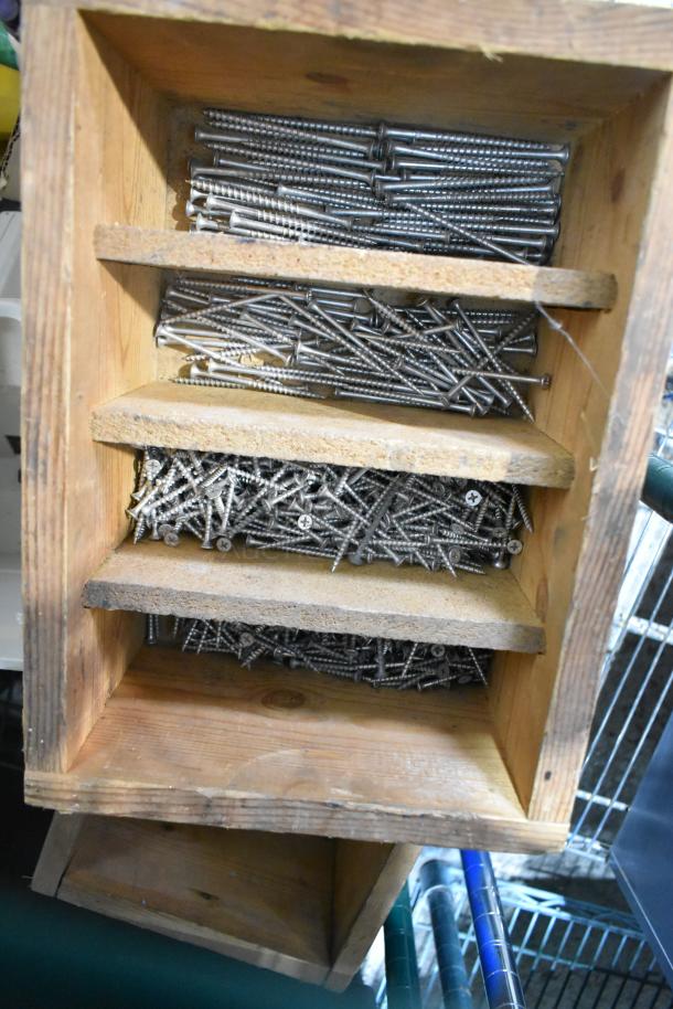 Wooden shelf with three compartments filled with various sizes of metal screws. Condition: Good.