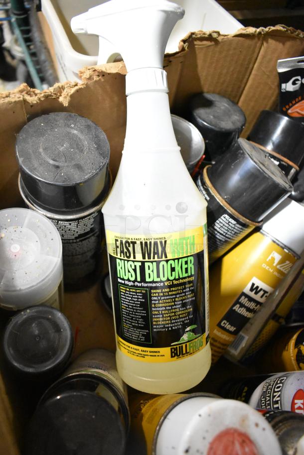 Box of various items including Bullfrog Fast Wax with Rust Blocker, adhesive cans, and cleaning sprays. Items show wear.