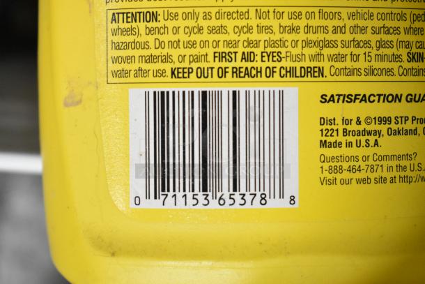 Yellow container close-up showing a barcode and safety instructions. Product by STP Products, made in the USA.