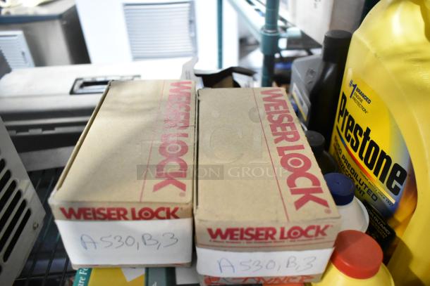 Boxes labeled "Weiser Lock," products like Prestone and other items on a shelf, indicating a mixed lot auction.