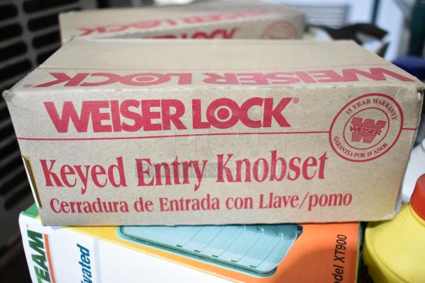 Weiser Lock Keyed Entry Knobset box with 15-year warranty printed, part of a lot including an air conditioner and other items.