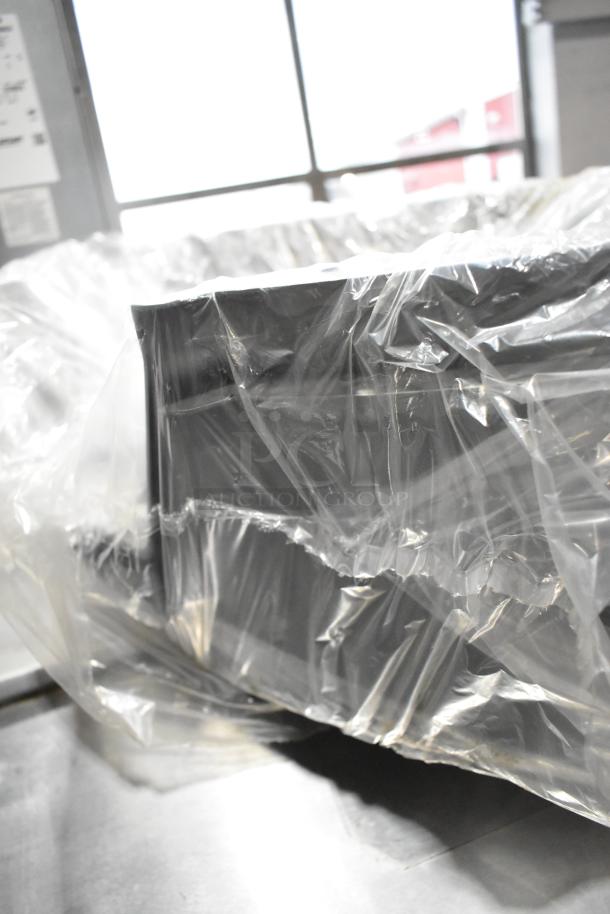 Plastic-wrapped black cat box, in new condition, partially visible in front of a window.