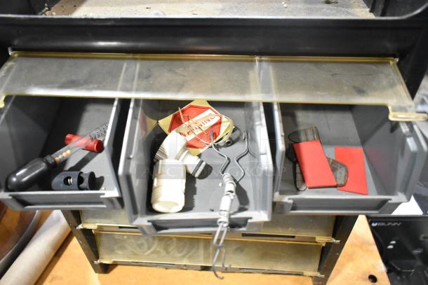 Poly hardware holder with multiple bins containing various small tools and hardware items, visible wear and dust.