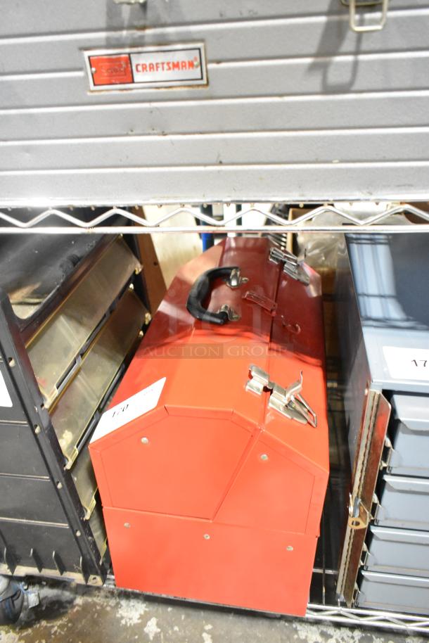 Red metal tool box with black handle and dual latches, containing assorted tools. Slight wear visible.