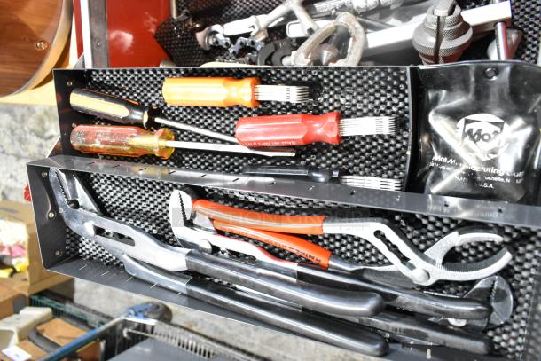 Red metal tool box with assorted hand tools, including pliers and screwdrivers, on a textured black interior.