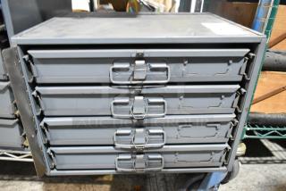 Gray metal 4-drawer hardware box, sturdy design, visible minor wear, suitable for organizing tools and parts.